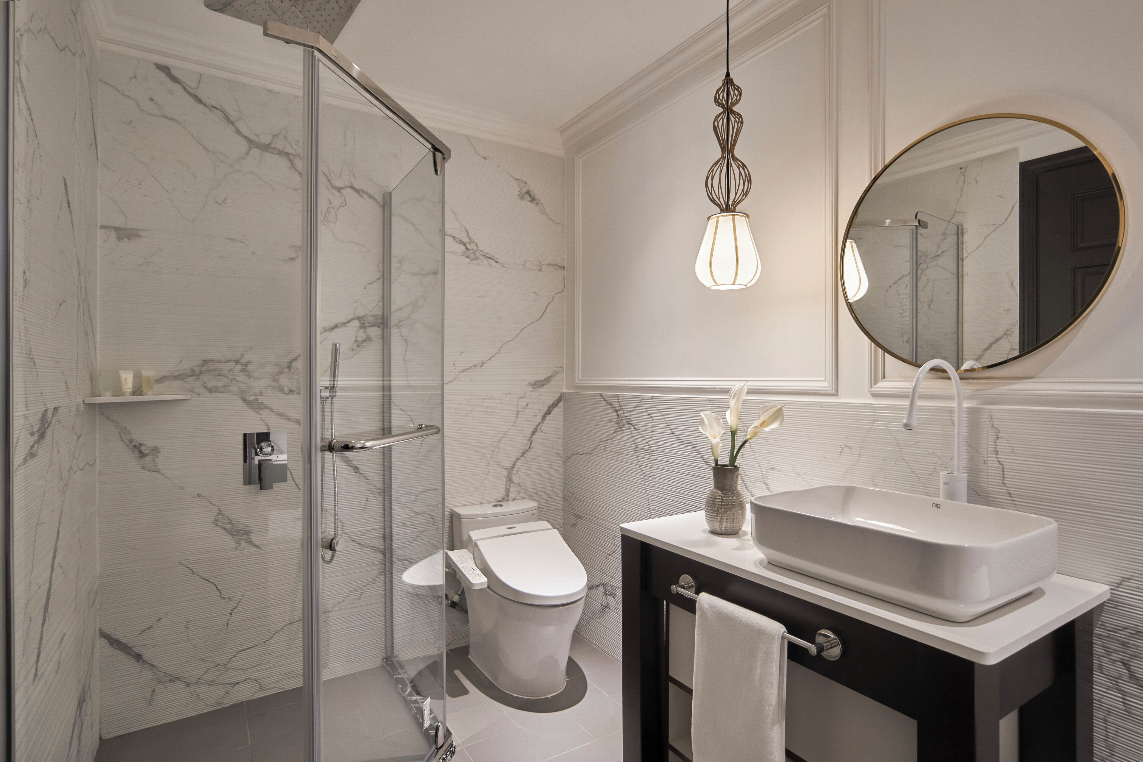 A modern bathroom with a glass shower enclosure, a toilet, a sink with a mirror, and a hanging light fixture.