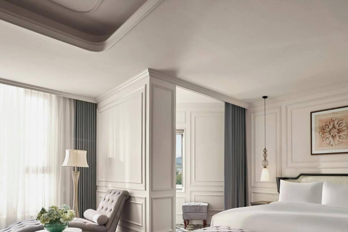 A hotel room with a large bed, a nightstand, a lamp, and a view of the outdoors.