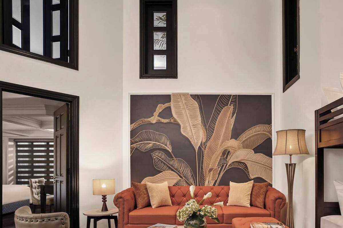 A hotel room with a bed, a sofa, a lamp, a wall art piece, and a door.