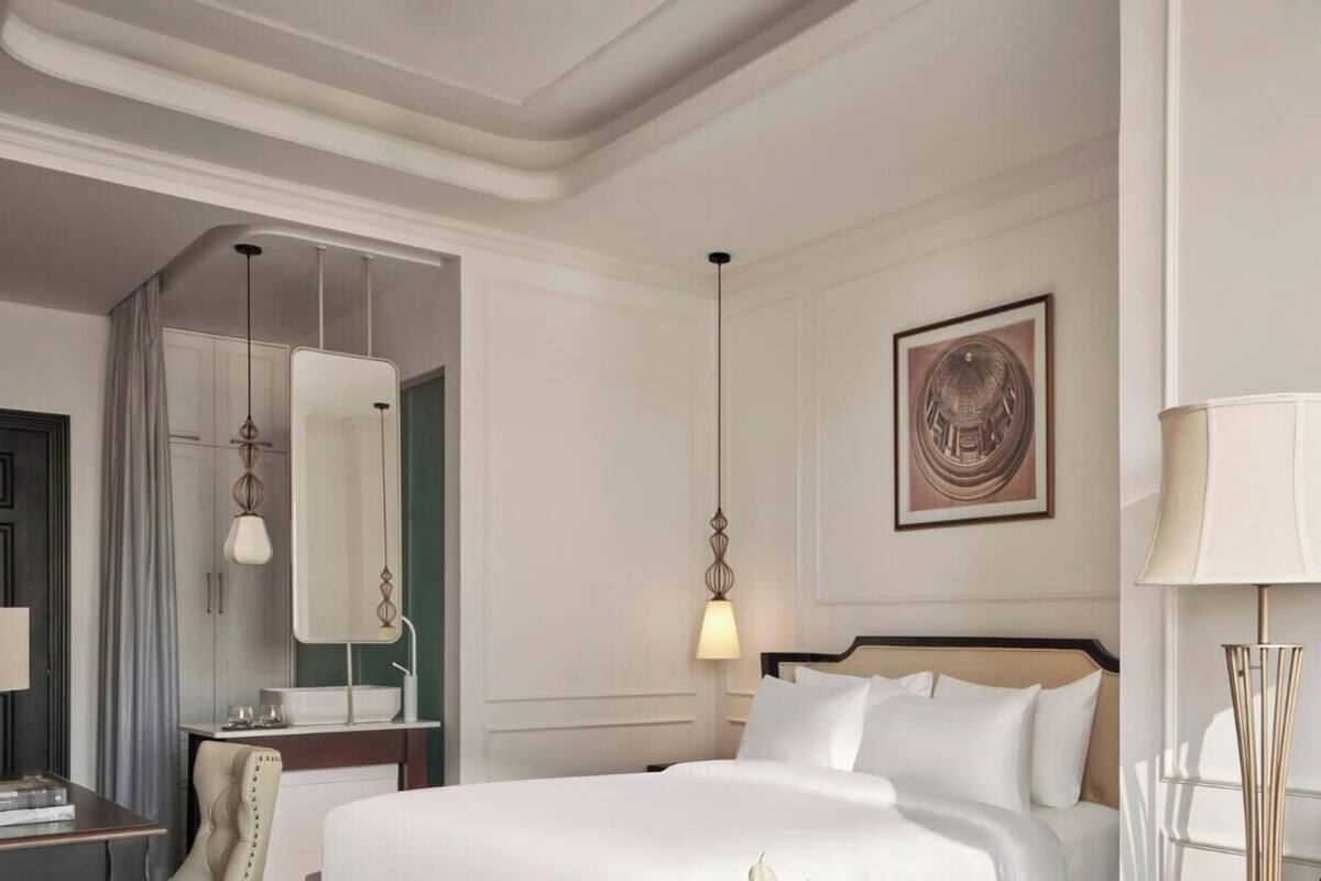 A hotel room with a bed, bedside table, lamp, and a painting on the wall.