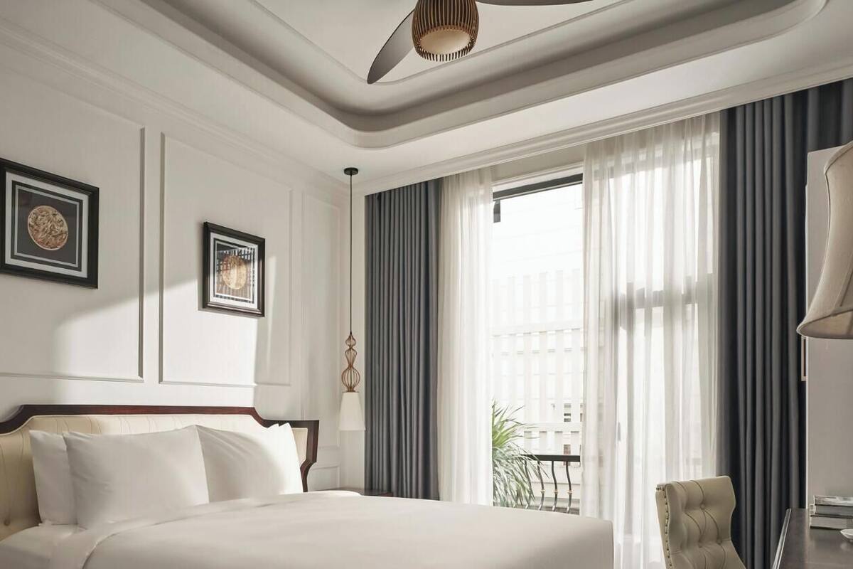 A hotel room with a bed, a chair, a table with a cup, and a window with curtains.