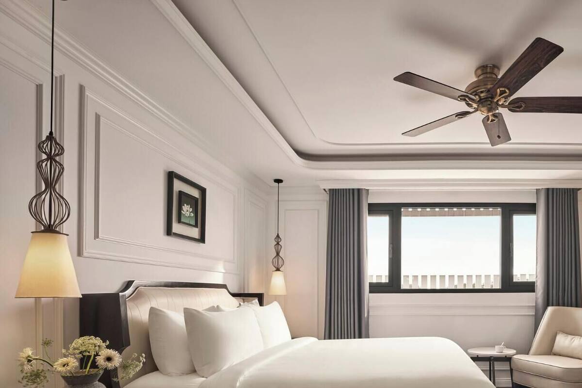 A hotel room with a bed, a chair, a desk, a television, a ceiling fan, and a window with curtains.
