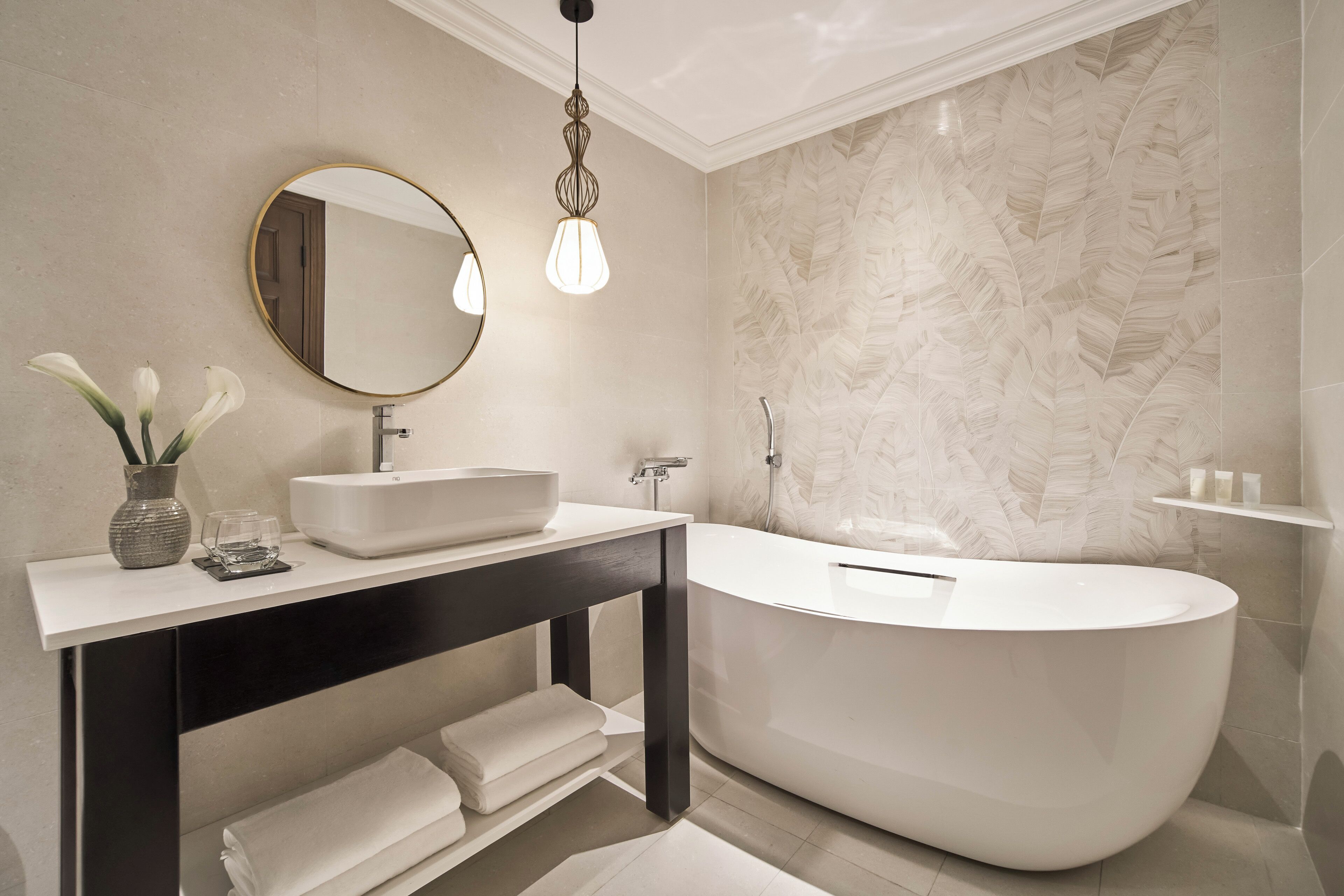 A modern bathroom with a freestanding bathtub, a round mirror, and a vase with flowers on a vanity.