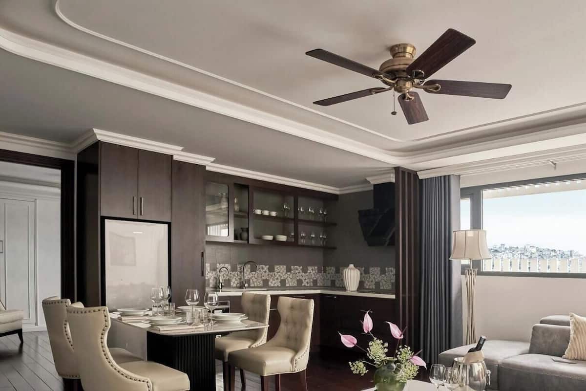 A modern living room with a dining area, a ceiling fan, a large window with curtains, and a view of the city.