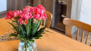 Une table à manger ornée d’un vase de fleurs roses, un meuble en bois et une lampe posée sur une étagère.