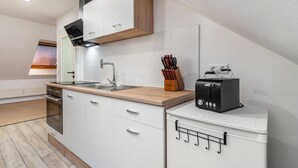 A modern kitchen with white cabinetry, a wooden countertop, a built-in oven, a black toaster, and a window with blinds. - Holiday Apartment 'Sena' with Balcony and Wi-Fi (Weisweil)