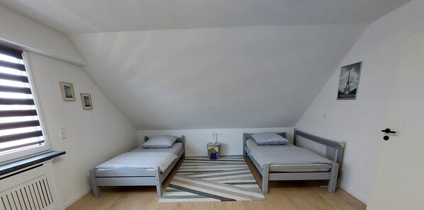A small, triangular attic bedroom with two single beds, a radiator, a window with blinds, and a picture of the Eiffel Tower on the wall.