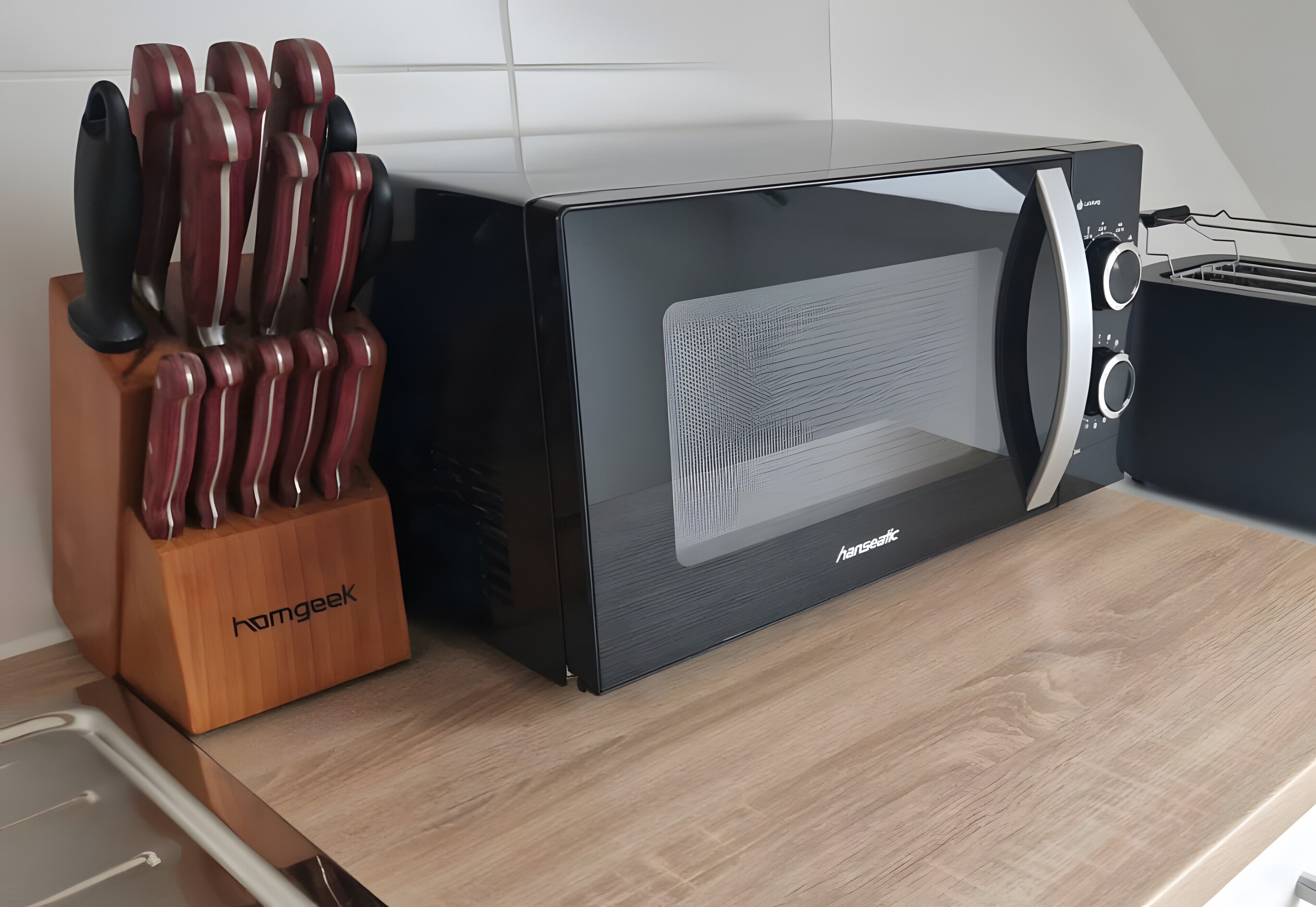 Een zwarte elektrische oven met een houten messenblok op een aanrecht.