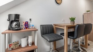 A kitchenette with a coffee maker, a kettle, and a coffee filter box. There is a wooden table with two chairs and a clock on the wall. - Holiday Apartment 'Sena' with Balcony and Wi-Fi (Weisweil)