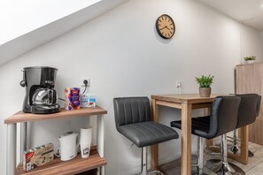 A kitchenette with a coffee maker, a kettle, and a coffee filter box. There is a wooden table with two chairs and a clock on the wall. - Apartment 'Sena' with Balcony and Wi-Fi (Weisweil)
