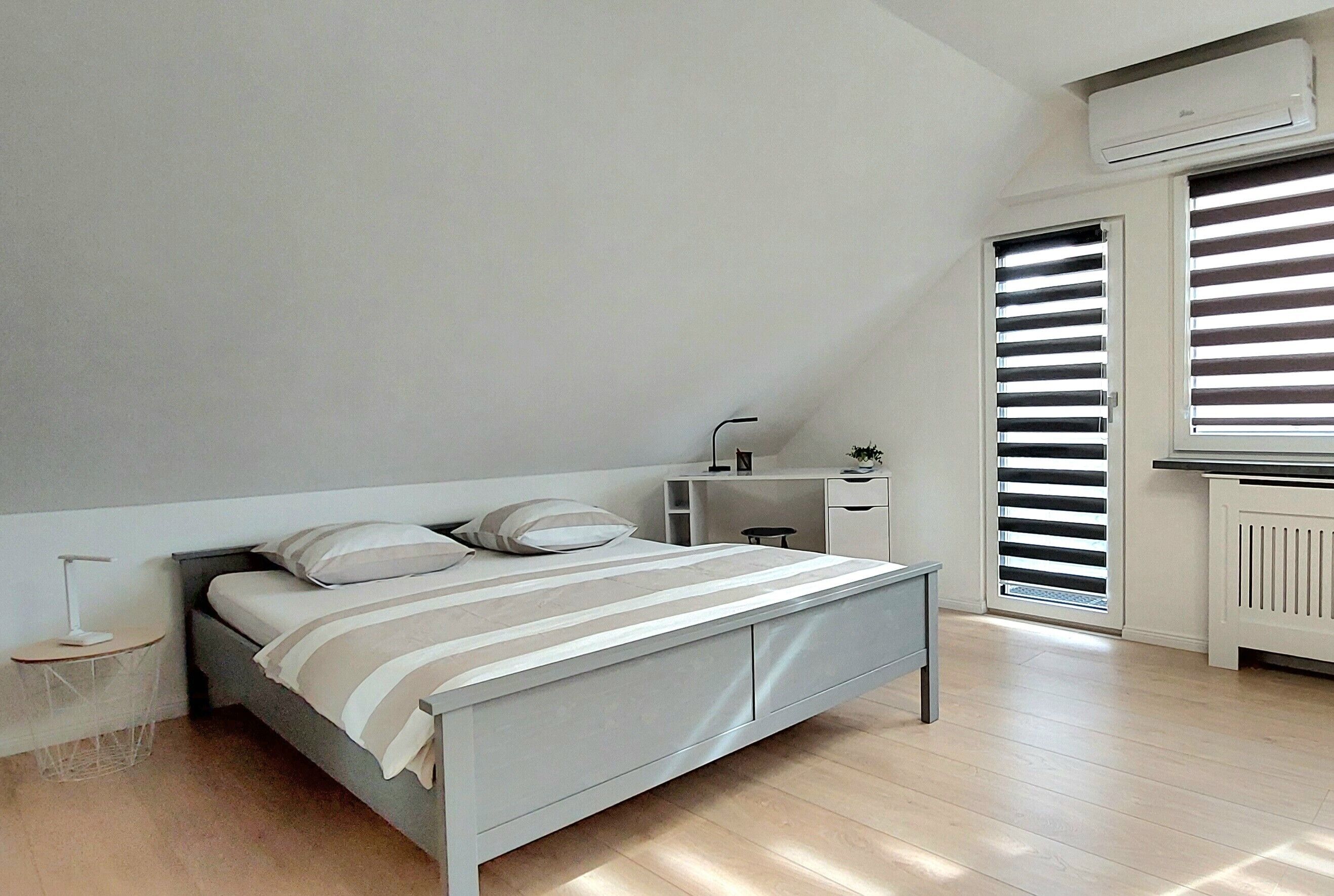 A bedroom with a bed, bedside table, lamp, and a window with blinds.