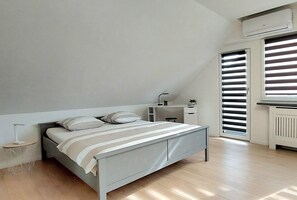 Un dormitorio con cama, mesita de noche, lámpara y ventana con persianas.