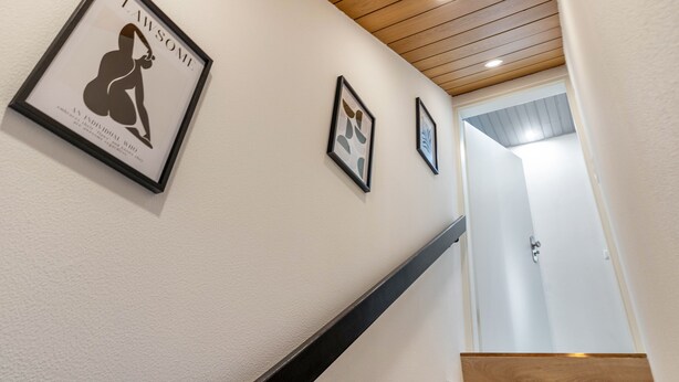 A hallway with framed artwork on the wall, a wooden staircase, and a door at the end. - Holiday Apartment 'Sena' with Balcony and Wi-Fi (Weisweil)