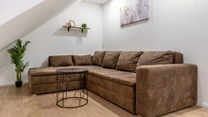 A sectional sofa, a small round table, a potted plant, a wall-mounted shelf with a picture, and a painting. - Holiday Apartment 'Sena' with Balcony and Wi-Fi (Weisweil)