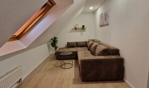 Una sala de estar moderna con un sofá modular, una mesa de centro redonda, una planta pequeña y una escalera de madera.