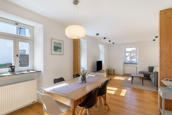 Una sala de estar moderna con una mesa de comedor de madera, sillas, un sofá y un televisor.