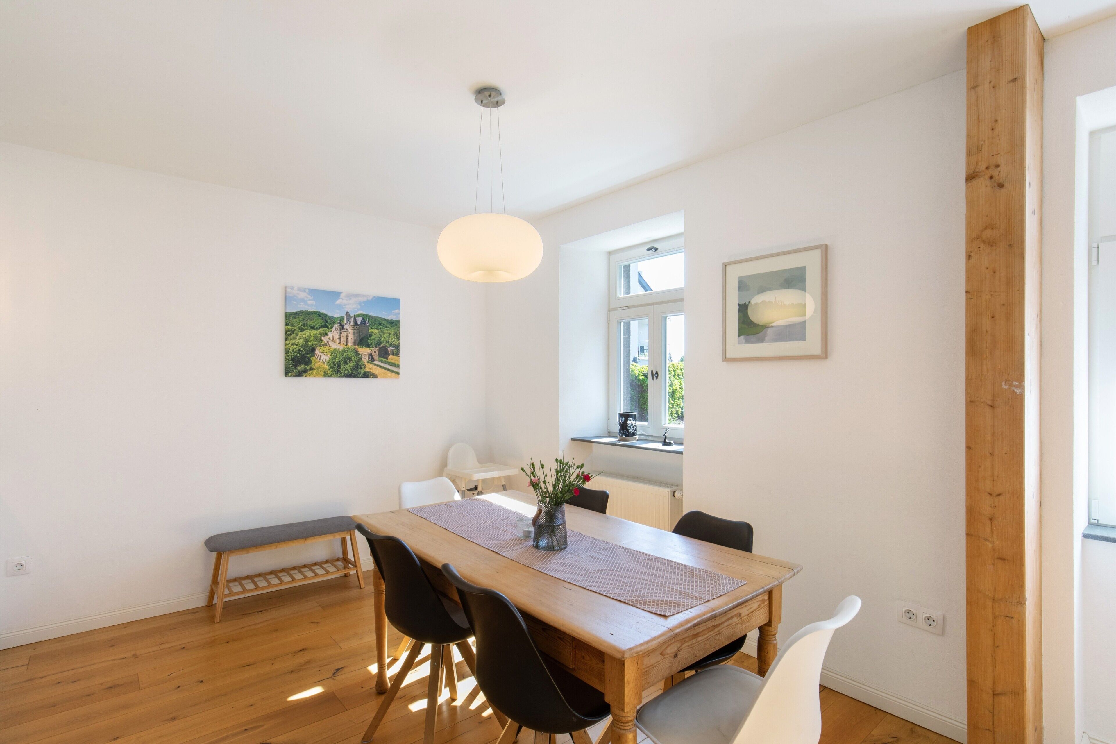 A dining area with a wooden table, black chairs, a bench, a hanging light fixture, and two framed pictures on the walls.