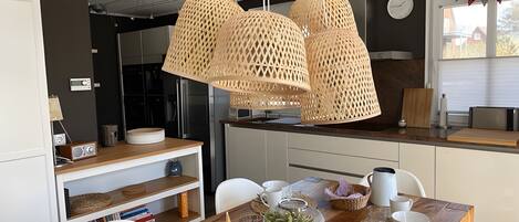 Una cocina moderna con una mesa de comedor de madera, sillas blancas y lámparas de ratán colgantes.