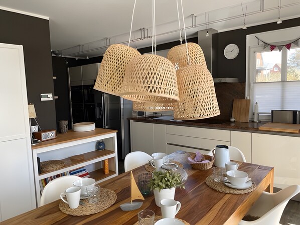 A modern kitchen with a wooden dining table, white chairs, and hanging rattan lamps.