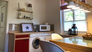 Een kleine keuken met een wasmachine, een magnetron, en een eethoek met een tafel en stoelen.