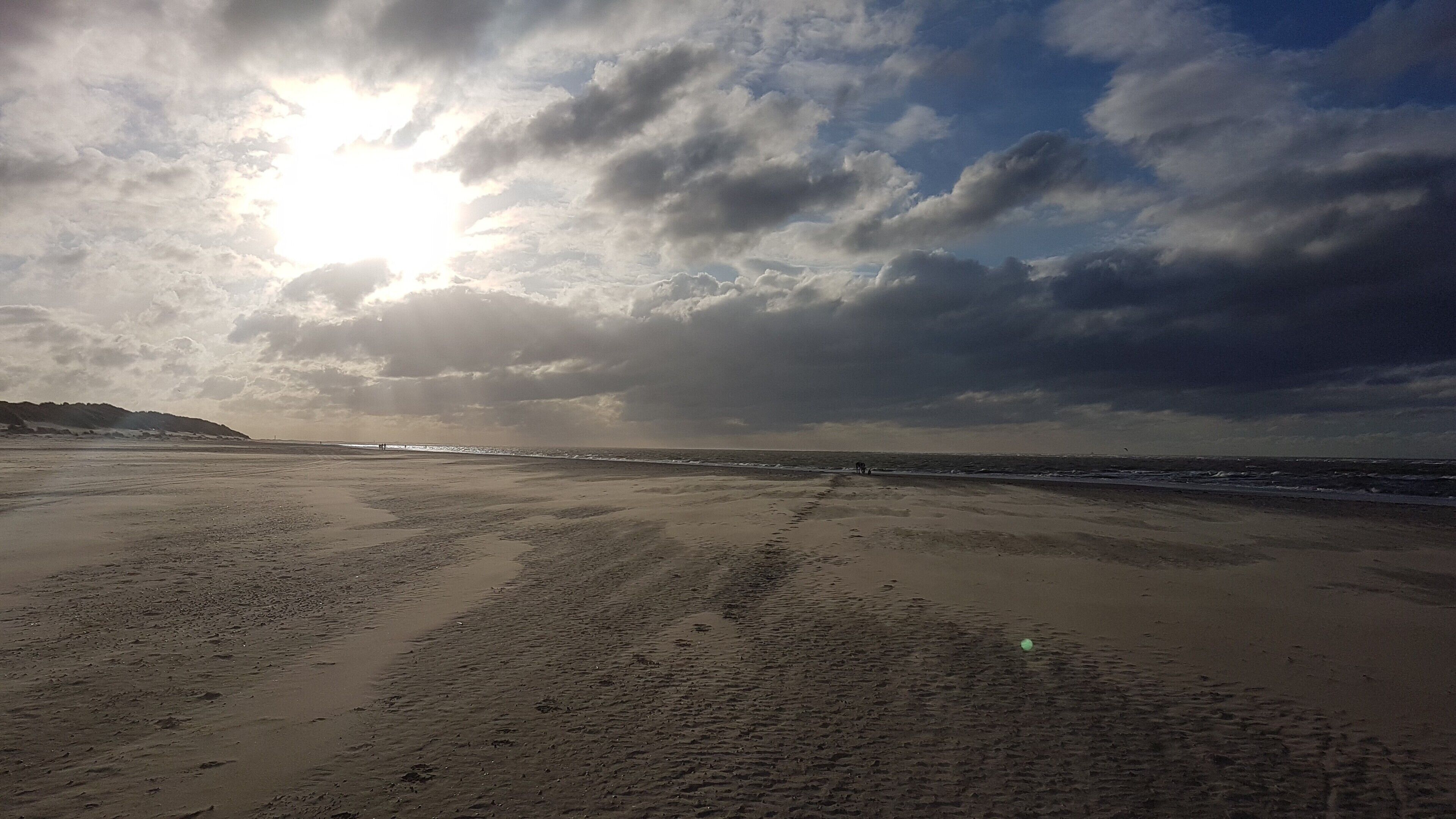 A beach with footprints leading to the water, a distant shoreline, and a cloudy sky.