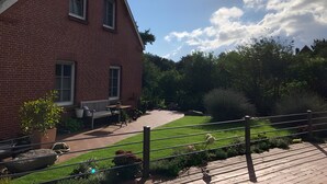 Een rode bakstenen woning met een geplaveid terras, een kleine tuin en een metalen hek.