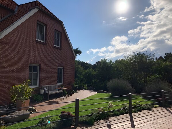 A red brick house with a paved patio, a small garden, and a metal fence.