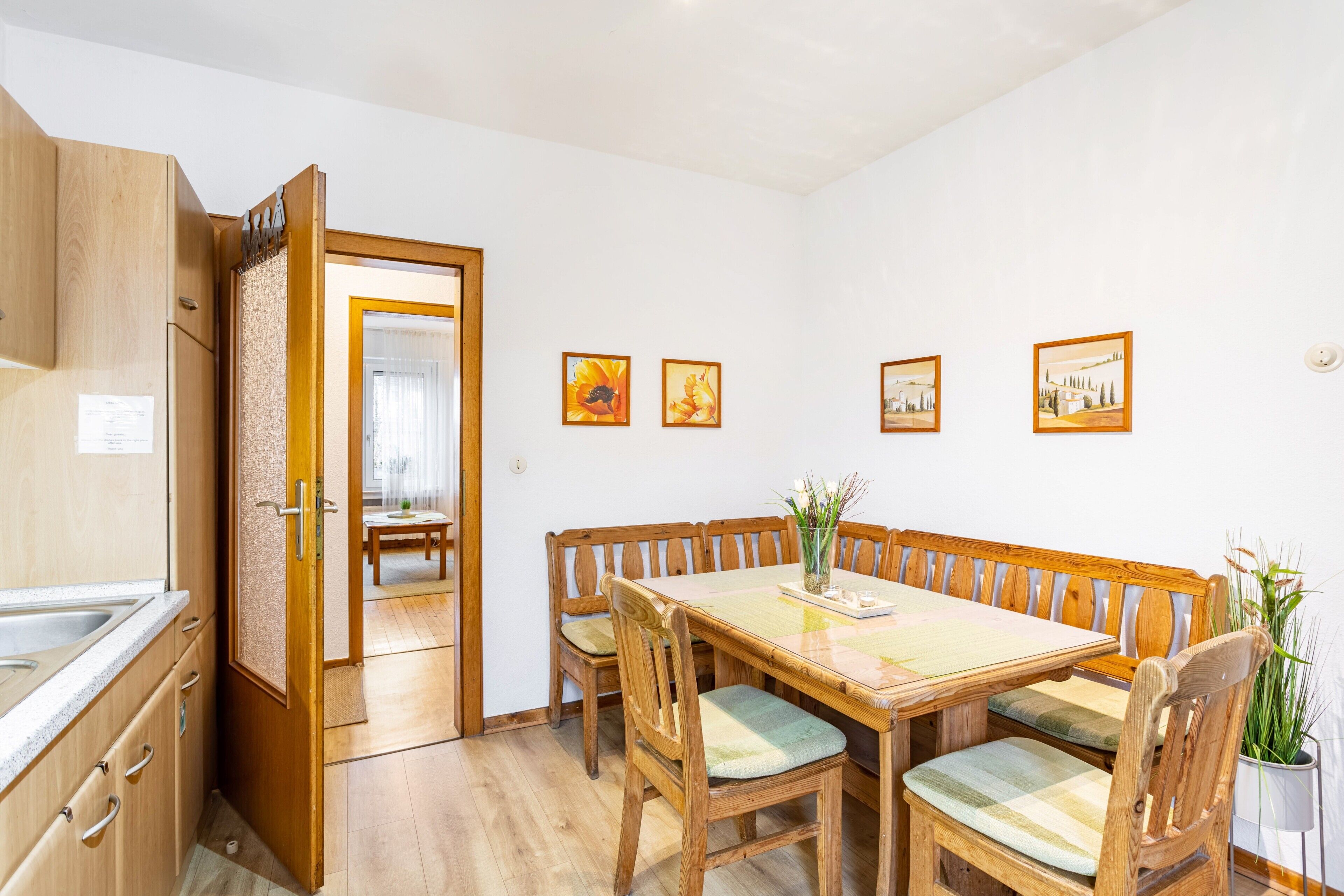 Un comedor con mesa y sillas de madera, una cocina con armarios de madera y una puerta que da a otra habitación.