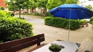 Un banco, una mesa con una planta en maceta y un paraguas azul en un jardín.