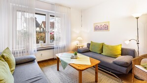 Una sala de estar con un sofá, una mesa con una planta, una lámpara y una ventana con cortinas.