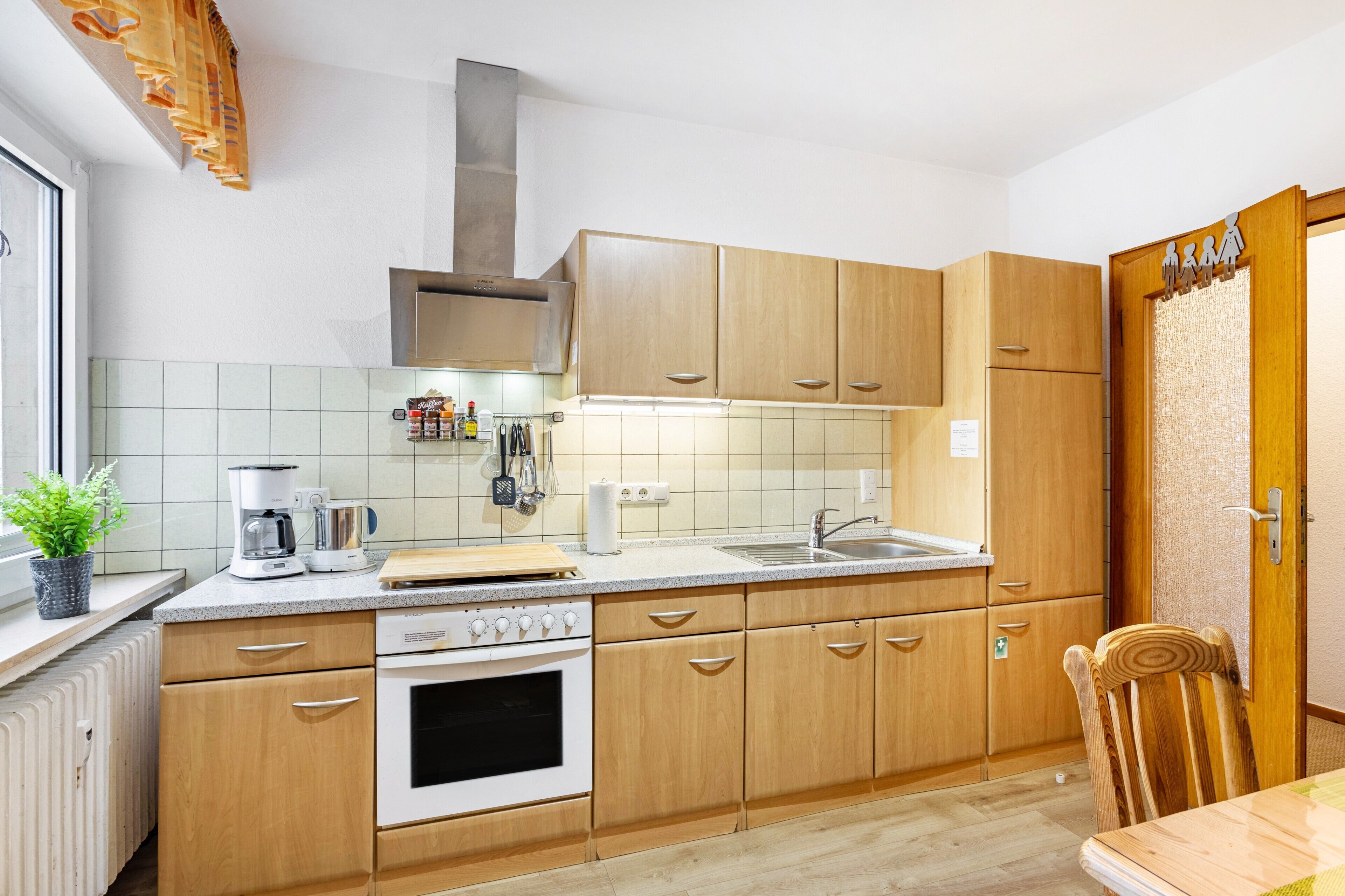 Une cuisine avec des meubles de rangement en bois, une cuisinière, un évier et une fenêtre sur le rebord de laquelle est posée une plante.