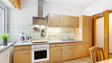 Une cuisine avec des meubles de rangement en bois, une cuisinière, un évier et une fenêtre sur le rebord de laquelle est posée une plante.