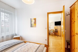 Une chambre à coucher avec un lit, une armoire en bois, un tableau, et une vue sur la cuisine et le salon.