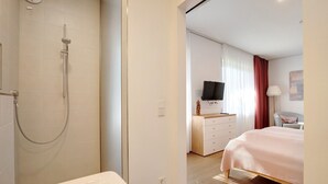 Habitación de hotel con ducha, cama, cómoda, televisor y escritorio.