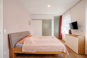 Une chambre à coucher comprenant un lit, un téléviseur, une commode et une porte coulissante.
