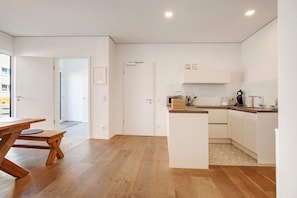 Une cuisine moderne avec un plancher en bois, des meubles blancs et un coin repas comprenant une table et un banc en bois.
