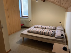 A bedroom with a single bed, a radiator, a window with blinds, a wooden wardrobe, and a small table with a lamp. - Apartment 'Käppeler' with Balcony and Wi-Fi (Salem)