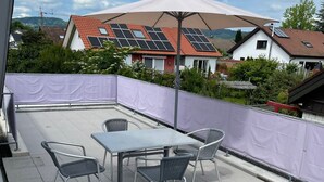 A rooftop patio with a table and chairs, solar panels on the roof, and a view of houses in the background.