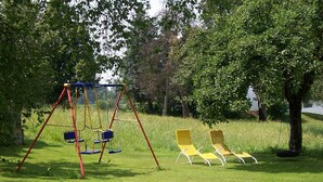 A swing set and two yellow lawn chairs in a grassy area with trees.