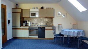 A compact kitchen with a dishwasher, stove, and microwave. There is a dining table with chairs and a small window above the sink.