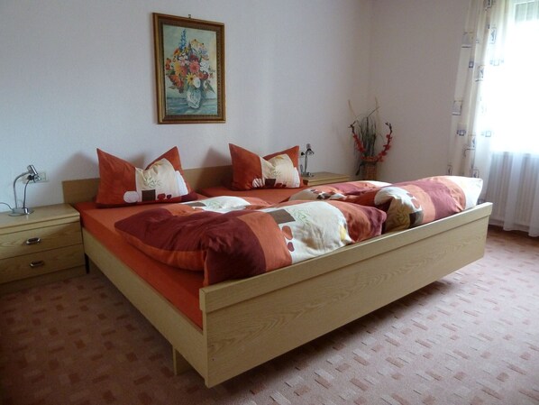 Une chambre à coucher avec un lit en bois, deux tables de chevet, une commode, un tableau au mur et une fenêtre avec des rideaux.
