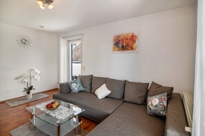 A modern living room with a sectional sofa, a glass coffee table, and a floral painting on the wall. - Apartment '01' with Shared Terrace, Balcony and Wi-Fi (Lindau)