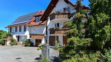 Ein zweistöckiges Gebäude mit einem geneigten Dach, Solaranlagen und einem Balkon mit Blumentöpfen.