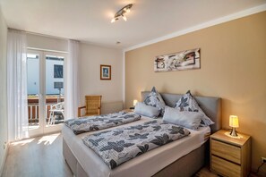 Una camera da letto con due letti, un comodino con una lampada, una sedia, una finestra con tende e un quadro appeso al muro.