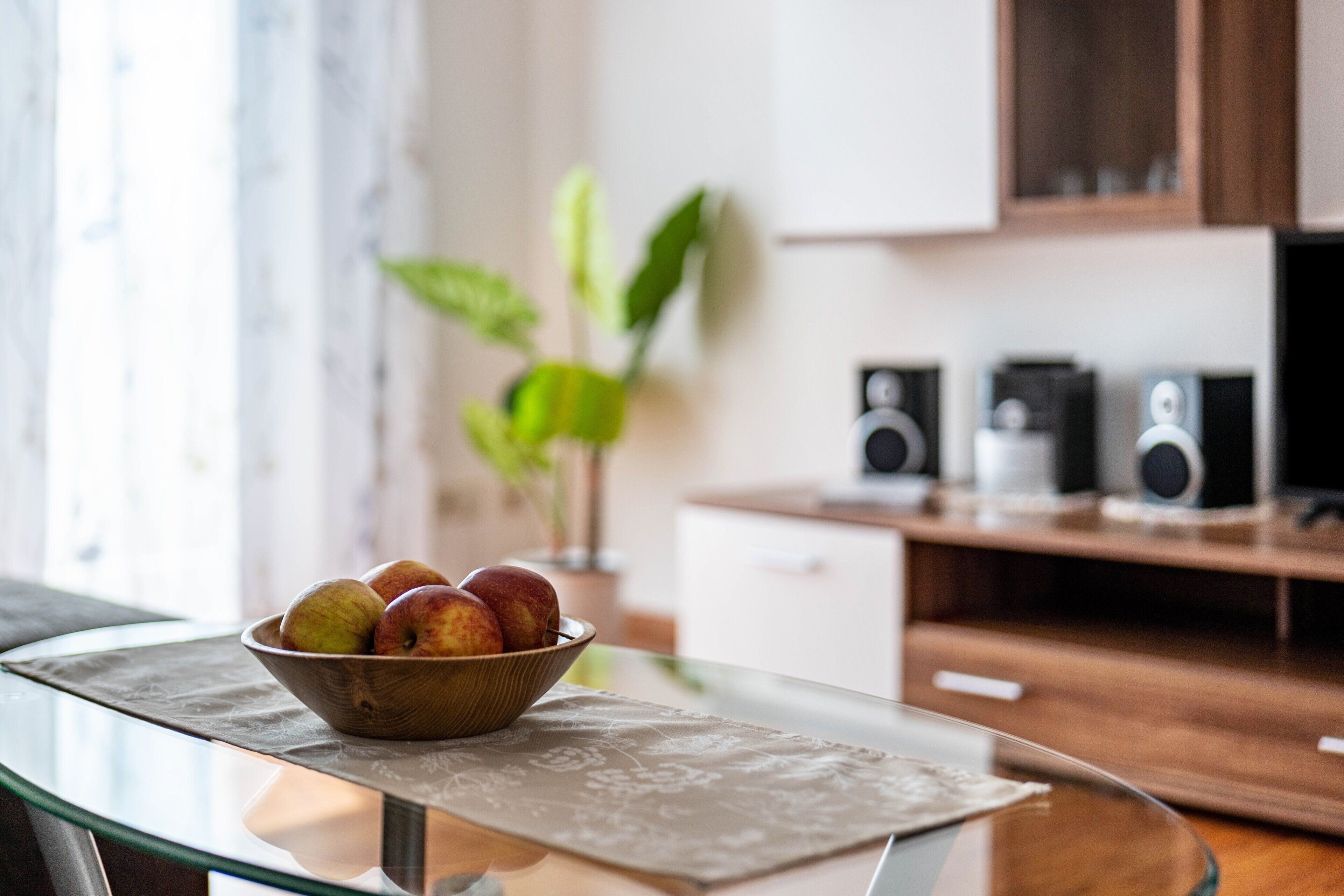 Mesa de vidro com uma tigela de frutas, uma planta e alto-falantes em uma cozinha moderna.