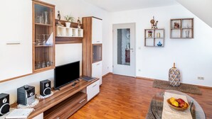A modern living room with a flat-screen TV, wooden entertainment unit, and a glass coffee table with fruit. - Apartment '02' with Shared Terrace, Balcony and Wi-Fi (Lindau)