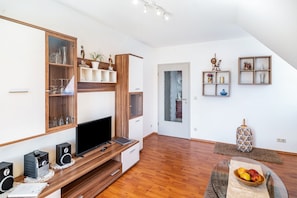 Un salon moderne doté d’un téléviseur à écran plat, d’un meuble de rangement en bois et d’une table basse en verre sur laquelle sont disposés des fruits.