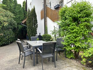 A patio with a table and chairs, surrounded by greenery and a building. - Apartment '02' with Shared Terrace, Balcony and Wi-Fi (Lindau)