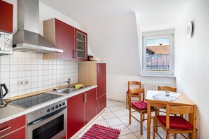 Une cuisine compacte équipée d’une cuisinière, d’un évier et de meubles de rangement rouges. On y trouve également un coin repas avec une table et des chaises.