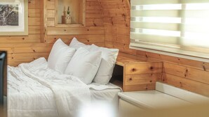A wooden cabin-style bedroom with a bed, pillows, a nightstand, and a window with blinds.